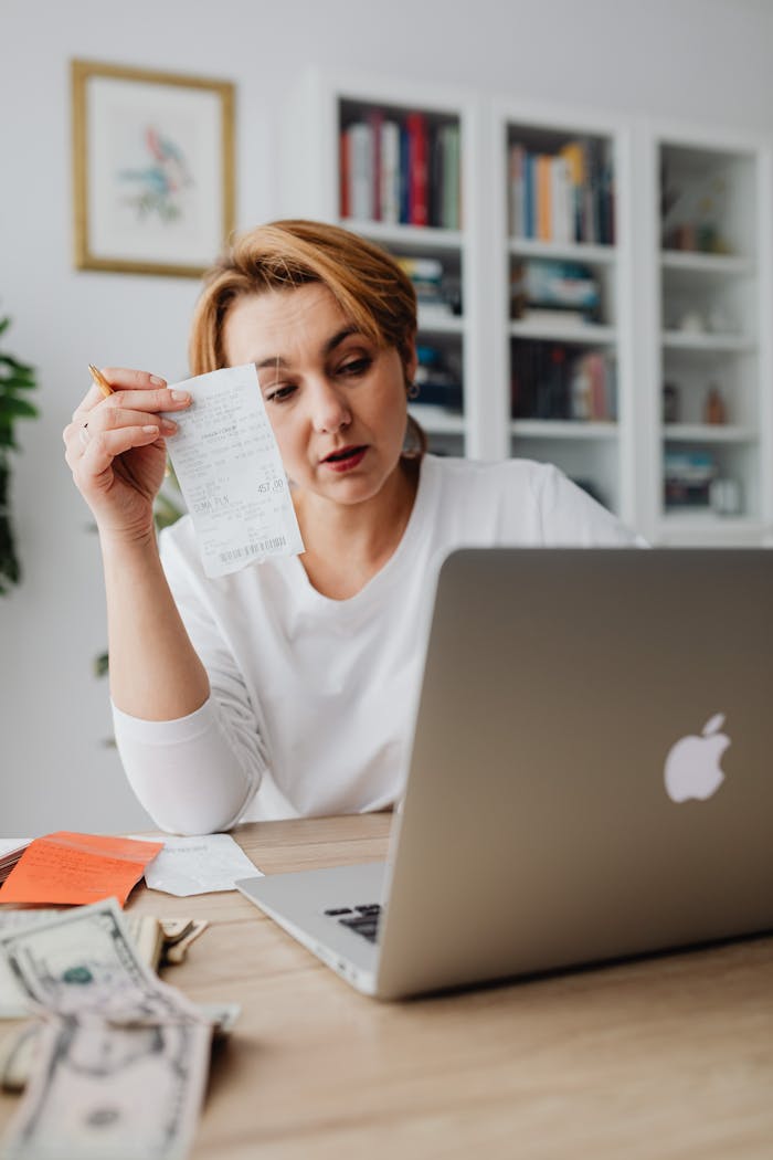 Woman using laptop while managing finances with receipts and cash on the table.